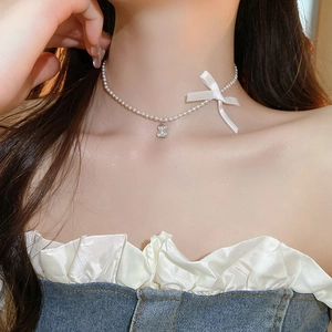 Close-up of pearl necklace with white bow and cute bear pendant on female neck