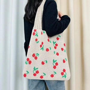 Detailed view of beige knitted tote bag with cherry patterns worn on shoulder