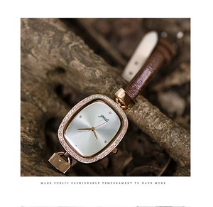 Detail of rose gold oval watch with diamond bezel and brown leather strap on wood