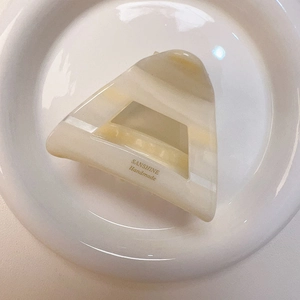 Dettaglio della molletta a triangolo in acetato marmorizzato crema con logo dorato