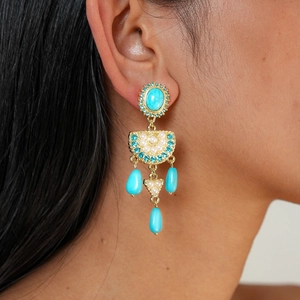 Close-up of bohemian gold earrings with blue stones and pearls on a female model