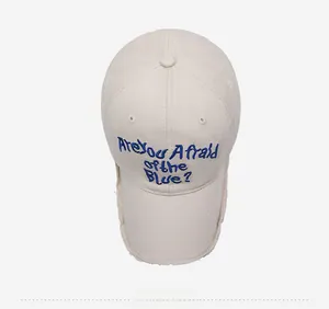 Detail view of beige distressed cotton baseball cap with blue embroidered lettering