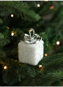 Macro view of white glitter foam gift box ornament with silver bow on a Christmas tree