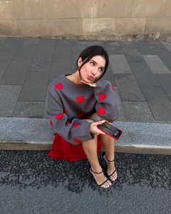Detail of grey crewneck sweater with red heart patterns showing loose knit fit on model
