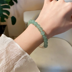 Detail of green aventurine beaded bracelet on wrist with elegant white pleated sleeve
