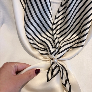 Elegant gold metal scarf buckle with double pearls on a black and white striped silk scarf