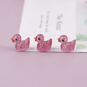 Close-up of three pink glitter resin duck miniatures in a row on a lavender backdrop