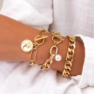 Detailed shot of layered gold coin bracelets with pearl accents on a white linen sleeve