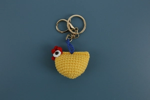Macro detail of handmade crochet yellow chicken keychain with golden metal ring and hook