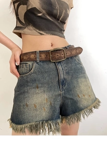 Close-up of vintage embossed brown leather belt with brass buckle on denim shorts