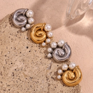 Detailed view of spiral earrings with pearls on textured stone in gold and silver finish