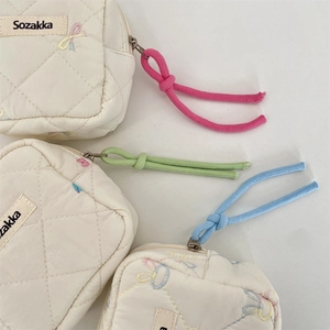Detailed macro of quilted cotton pouch featuring embroidered details and colorful rope zippers