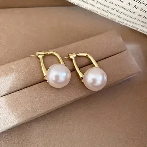 Elegant gold U-shape pearl drop earrings on beige velvet jewelry display stand