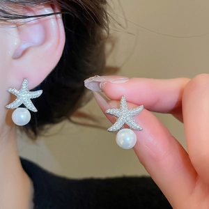 Détail de boucles d'oreilles étoile en zircon avec perle blanche sur clou argent