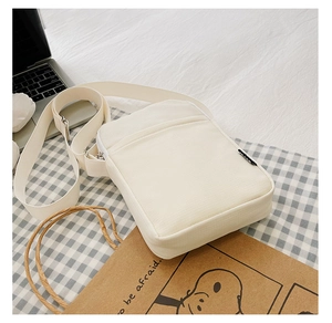 Detail of a minimalist white canvas crossbody phone bag on a black and white checkered fabric