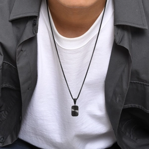 Detail of men's matte black square pendant necklace with radial texture on a model