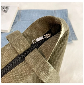 Detail of army green canvas tote bag showing black zipper and metal hardware close-up