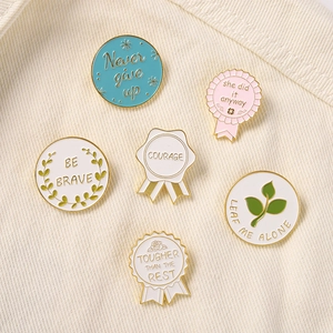 Close-up of enamel pins set with motivational quotes on a beige textured fabric