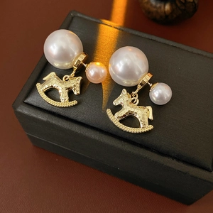 Golden rocking horse earrings with large white pearls shown on a black jewelry box