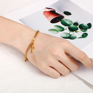 Dettaglio di un bracciale a doppia catena dorata con pendente a croce indossato da una modella
