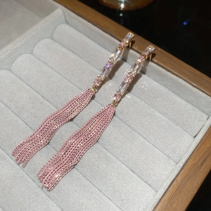Macro detail of long tassel earrings with pink zircon stones on grey velvet display