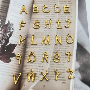 Goldene Buchstabenanhänger im Bambus-Stil A-Z auf einem offenen Vintage-Buch
