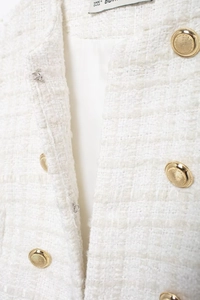 Detailed macro view of white tweed fabric and textured gold buttons on sleeveless vest