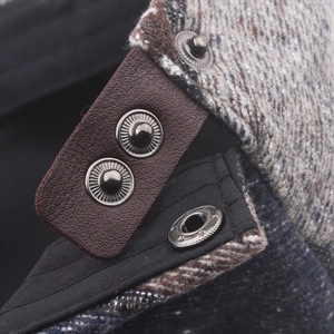 Macro detail of wool tweed newsboy cap featuring adjustable brown leather back strap