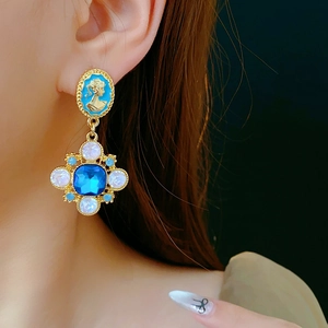 Detailed close-up of a vintage gold earring with blue cameo and inlaid crystals on ear