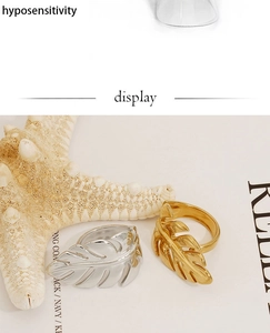 Detailed view of leaf-shaped stainless steel rings in gold and silver on a white background