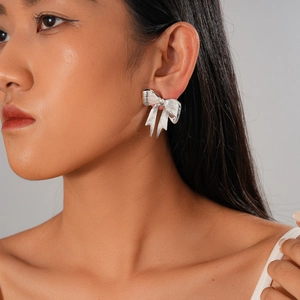 Metallic bow stud earrings in silver finish with textured stripes on model's ear