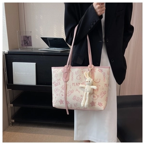 Close-up of a cream tote bag with pink graffiti patterns and a cute plush rabbit charm