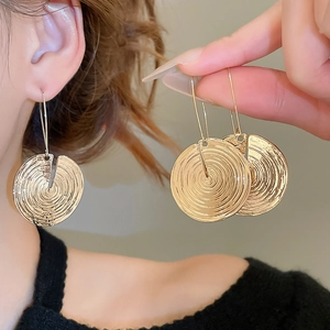 Detailed view of golden round spiral earrings showing metallic texture and model's fit