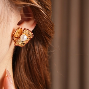 Detailed shot of a gold flower pearl earring with red trim on a model's ear