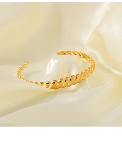 Detailed view of an 18K gold-plated twisted rope cuff bracelet on a soft silk background