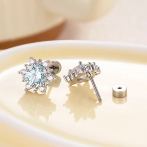 Silver snowflake zircon cartilage stud earrings with light blue center stone in a dish