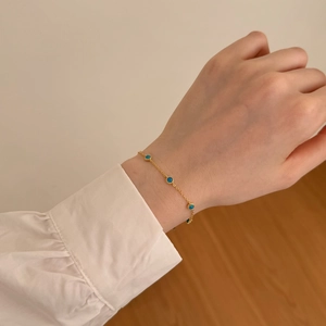 Detail of a minimalist gold bracelet featuring small round blue turquoise beads on wrist