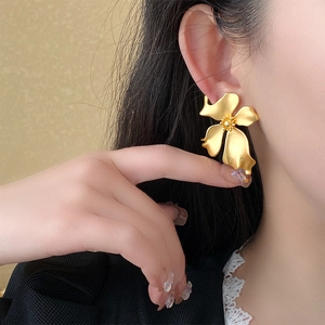 Close-up of a model wearing matte gold flower stud earrings in a vintage French style