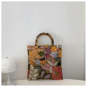 Macro detail of floral embroidery and beadwork on a green linen bag with bamboo handle