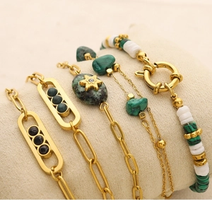 Detail of stacked gold bracelets featuring natural green stones and intricate chain links