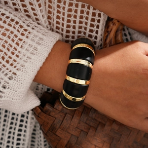 Détail d'un large bracelet en résine noire avec anneaux métalliques dorés au poignet