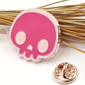 Pink skull enamel pin with rose gold plating and heart-shaped nose on white background