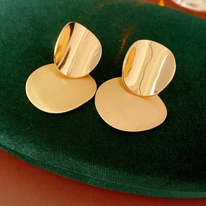 Close-up of golden geometric earrings featuring a brushed metal texture and mirror finish