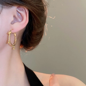 Close-up of a model wearing a gold star-studded hoop earring with dangling star charms