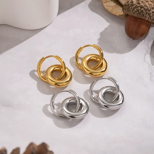 Close-up of interlocking gold and silver stainless steel hoop earrings on marble surface