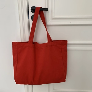 Detail of red canvas tote bag hanging on a white door handle showing soft texture