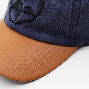Detail of navy washed denim baseball cap with black embroidery and brown PU leather brim