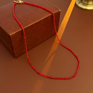 Détail d'un collier de cristaux rouges avec fermoir doré près d'une boîte en cuir vintage
