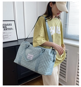 Detail of light blue quilted travel bag with adjustable strap shown on model shoulder