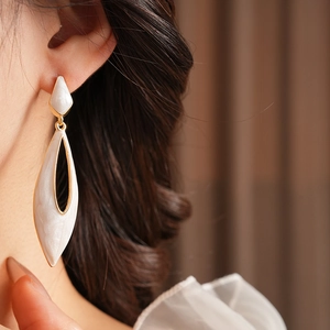 Close-up of a vintage white enamel teardrop earring with gold metal trim on model